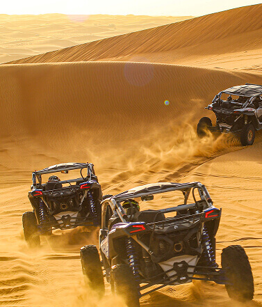 Dune buggies racing across desert sand at sunset